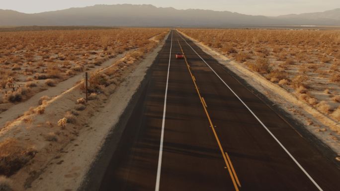 红色经典轿车沿着荒凉的沙漠公路行驶