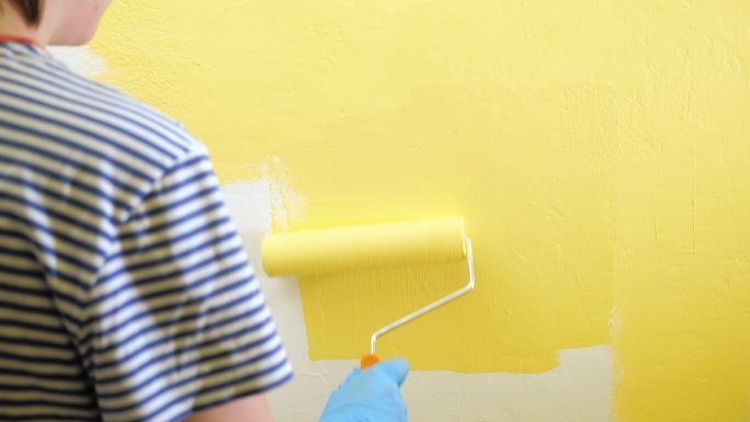 女孩用右手拿着滚筒把墙漆成黄色