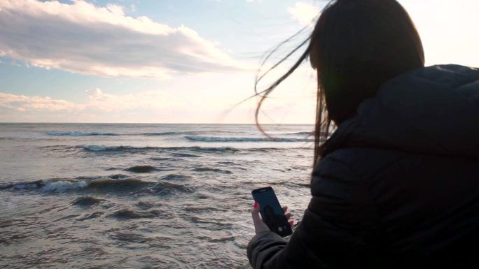 女郎坐在岩石海滩上用手机自拍