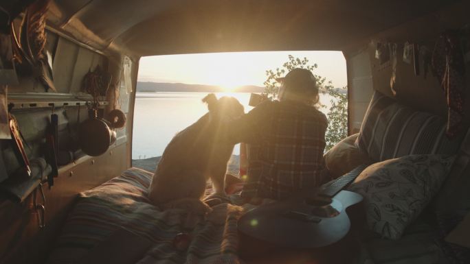 在面包车和爱犬看湖面日落的女人