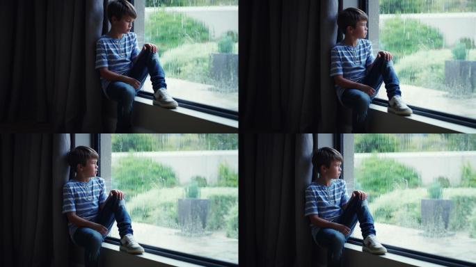 一个悲伤的小男孩在家透过窗户看雨