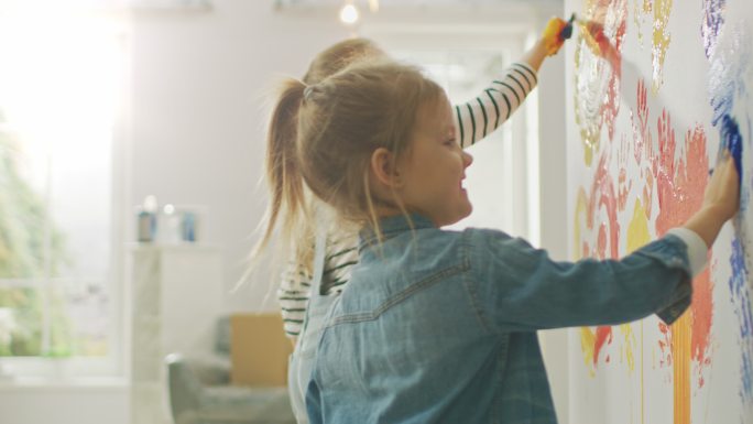 两个小女孩用手蘸着颜料在墙上画手印