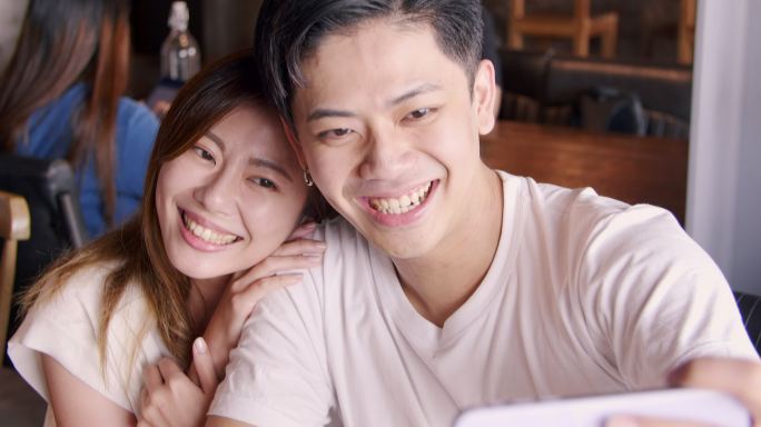 幸福的年轻夫妇在餐厅用手机拍照自拍