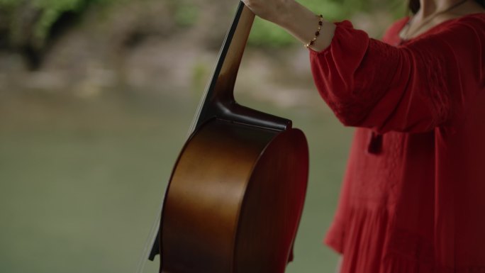 女孩在湖边瀑布前拉大提琴