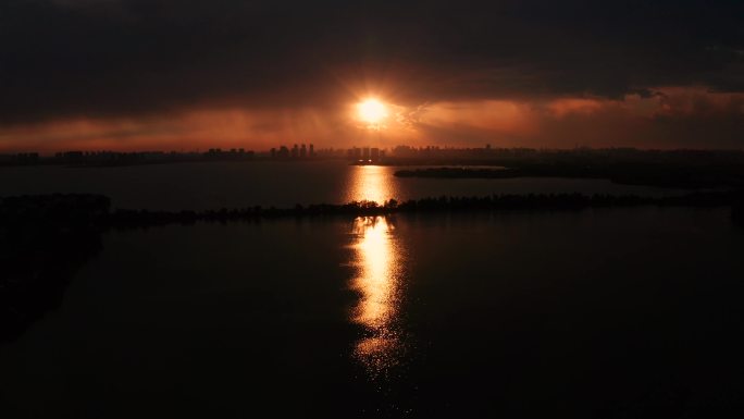 湖面上，夕阳穿过乌云压顶，将阳光洒向湖面