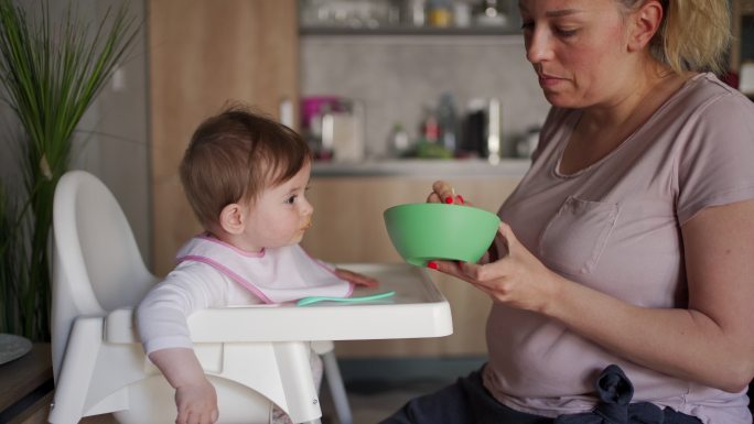 母亲用勺子给女婴喂有机胡萝卜泥