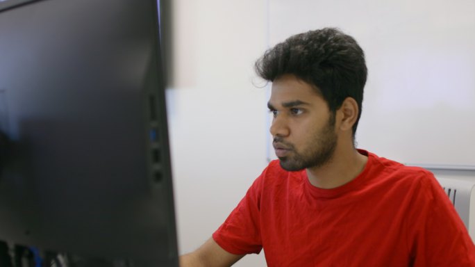 男学生坐在电脑桌旁的教室里工作