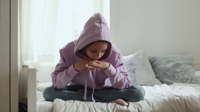 闷闷不乐的少女独自坐在床上思考问题