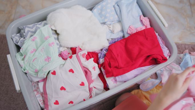 母亲在家里整理旧的婴儿衣服，放入捐赠箱。