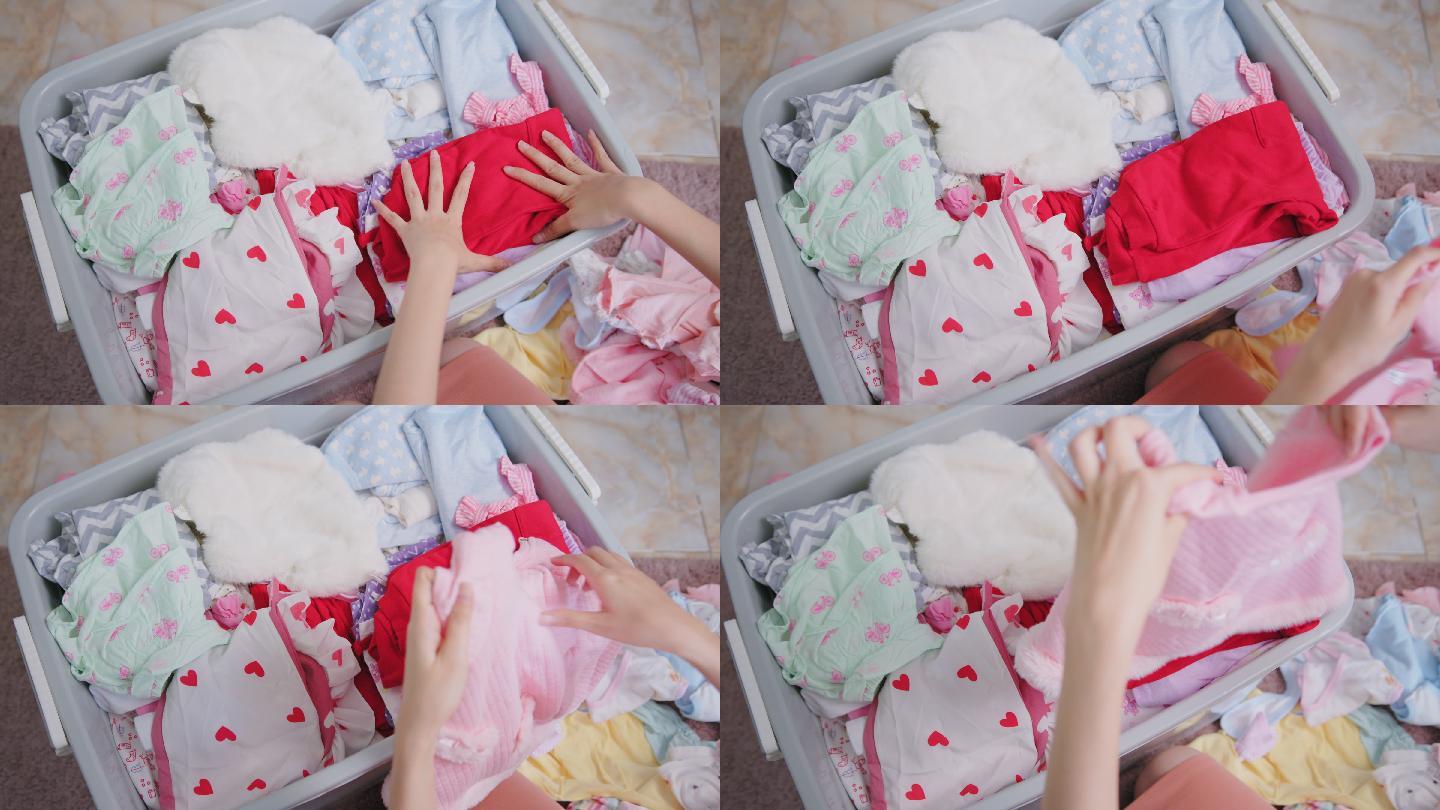 母亲在家里整理旧的婴儿衣服，放入捐赠箱。