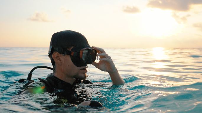 一名戴水肺的潜水员在日落时从水中浮出水面