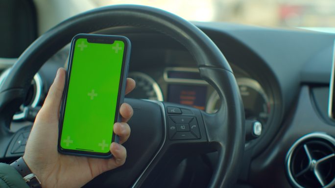 在汽车中，一名男子使用绿色屏幕智能手机