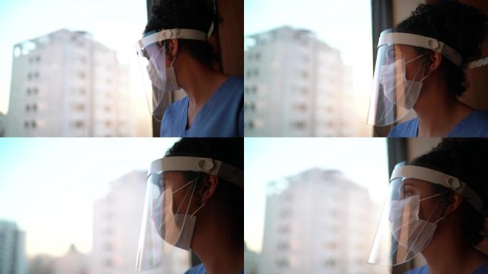 戴着防护口罩的护士透过医院的窗户看