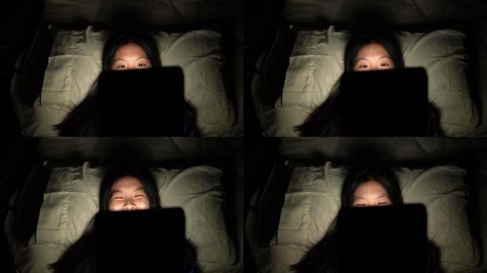 女性仰卧在黑暗的卧室里使用数码平板电脑