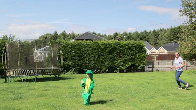 男孩穿着恐龙的衣服，被他的祖母在花园里追