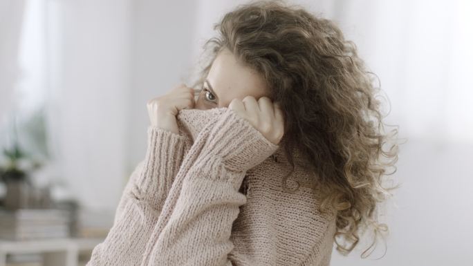 害羞的女人用针织毛衣遮住脸