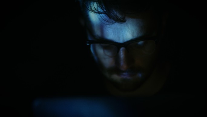 戴眼镜的人在黑暗中阅读平板电脑