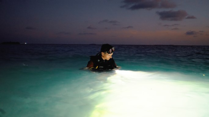 潜水员在黄昏时用手电筒在水中搜寻