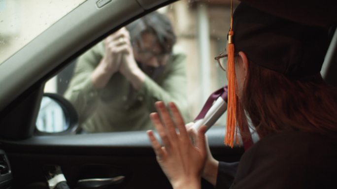 女孩穿着毕业礼服与车外的男子打招呼