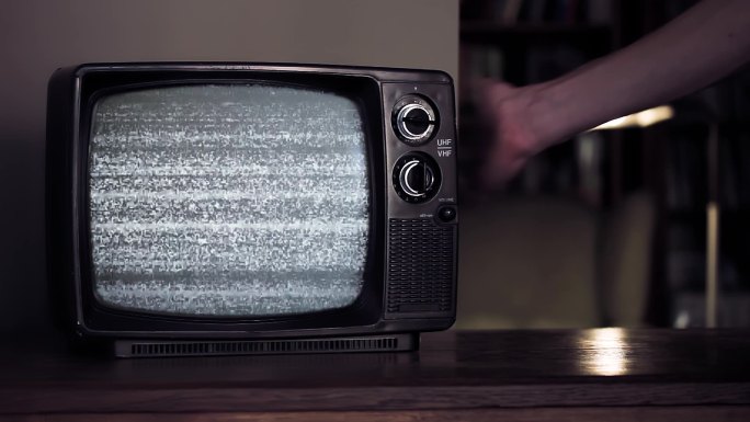 男性用手拍打一台绿色屏幕的旧电视机。