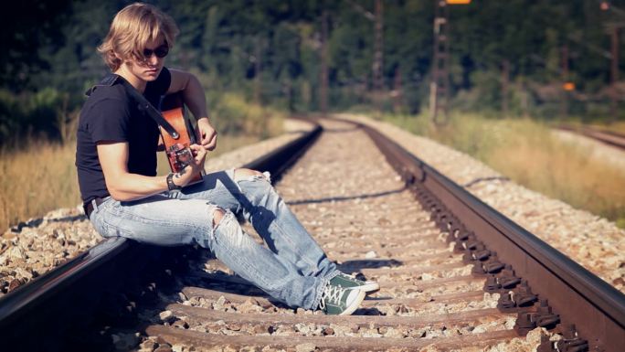 吉他手坐在铁轨上弹奏