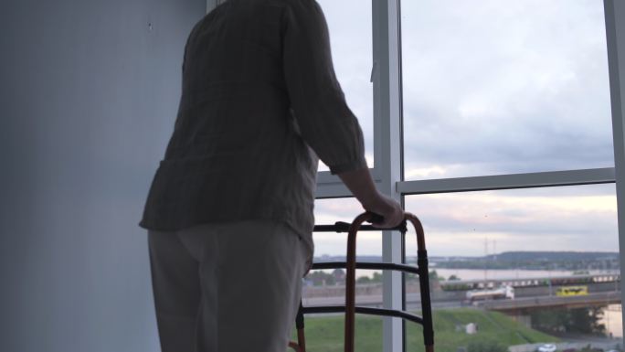 残疾的老妇人带着辅助器走近窗户