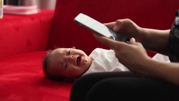 婴儿在哭泣，母亲在旁边玩手机