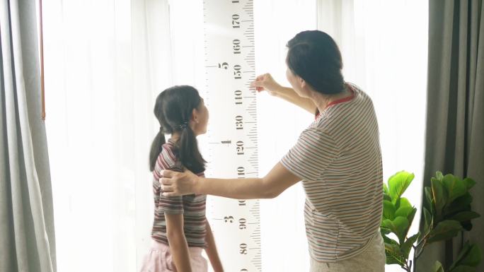 母亲通过测量仪器测量女儿的身高。