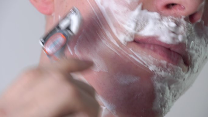 一个年轻人在浴室里用剃须刀刮胡子