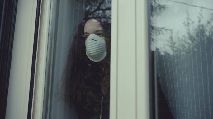 年轻女子戴着口罩，从窗户向外看