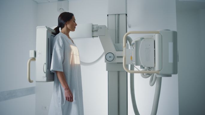 女性穿着医用长袍站在X光机前检查