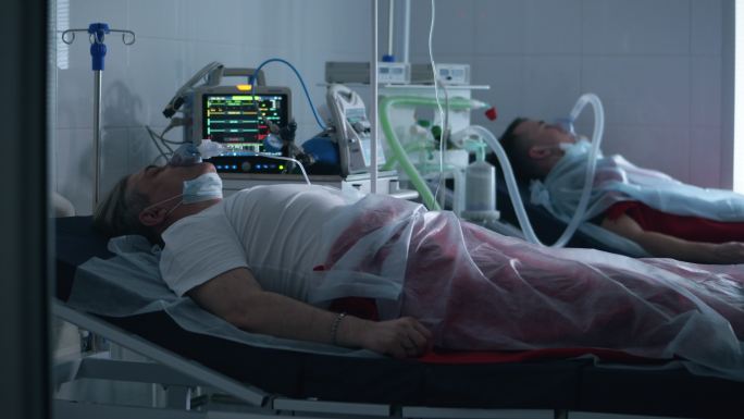 两名男子躺在医院里，用呼吸机呼吸。