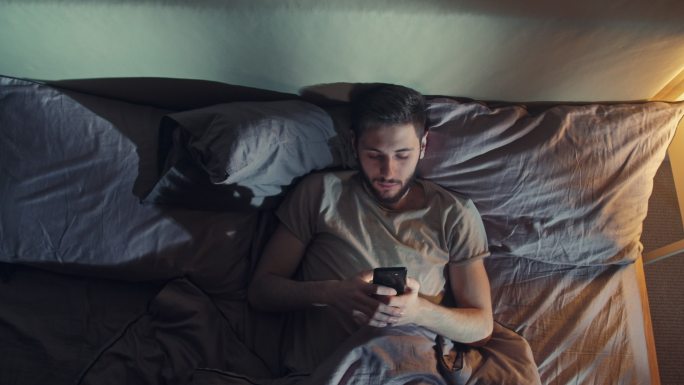 无聊的男人睡觉前使用智能手机。