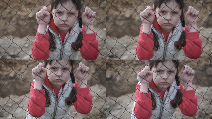 悲伤的孩子躲在铁栅栏后面。