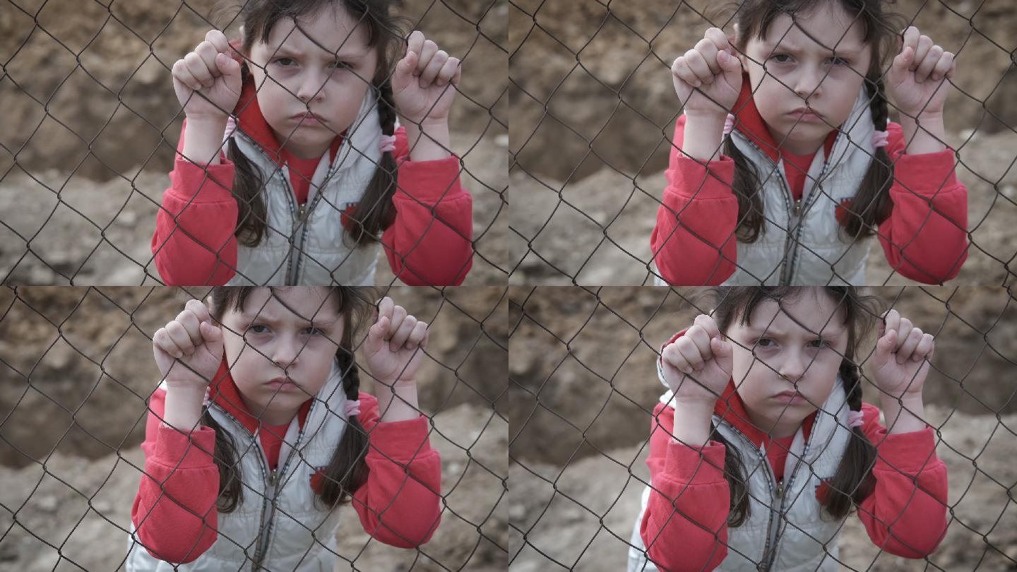 悲伤的孩子躲在铁栅栏后面。