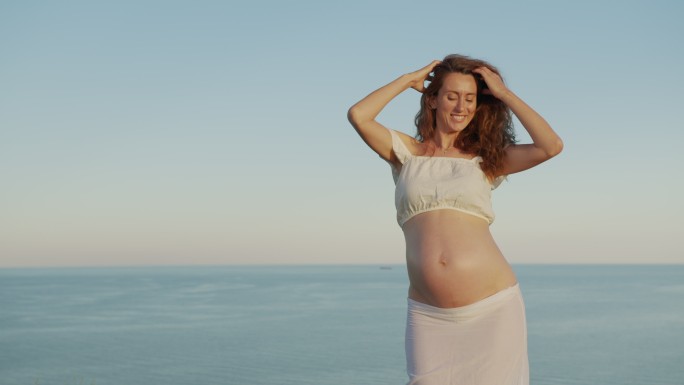 怀孕的女人在海边尽情跳舞。