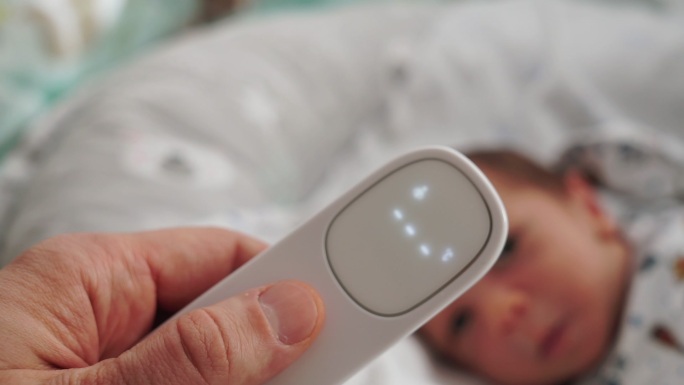 母亲用数字非接触温度计测量婴儿体温。