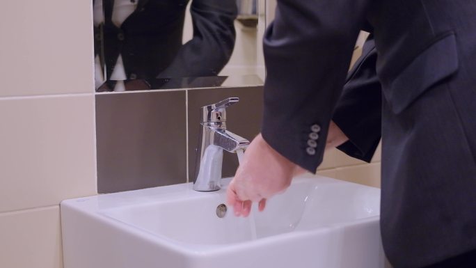 一名穿着西装的男子在公共办公室厕所洗手