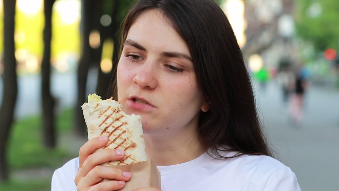 女人在城市的街道上吃着沙瓦玛