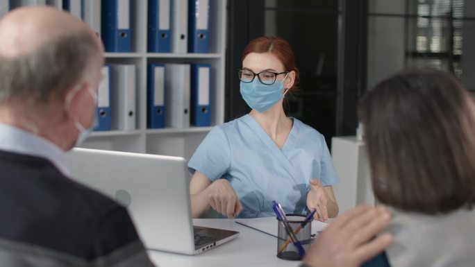 戴着医用口罩的女医生在医院办公室接待病人