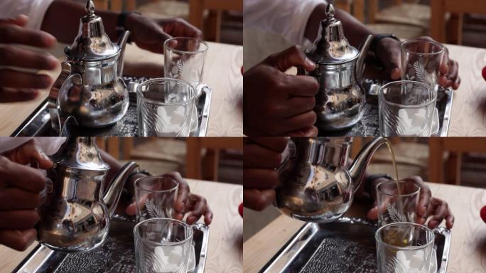 男子将银茶壶中的茶倒进小桌上的玻璃杯中。