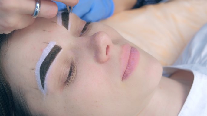 在美容院，美容师用镊子在女人脸上拔眉毛。