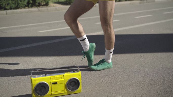 年轻人站在路边播放黄色复古录音机做运动。