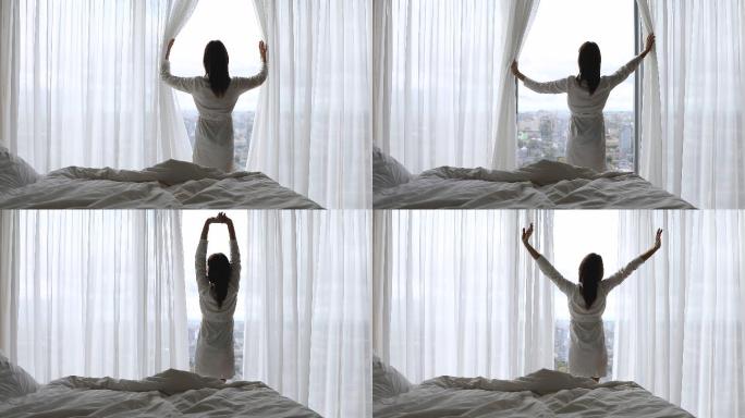 快乐的女人从床上起来打开窗帘