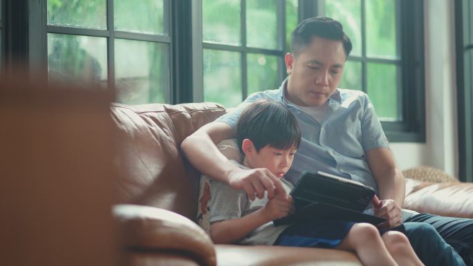 男孩和父亲在家里的客厅里一起使用平板电脑