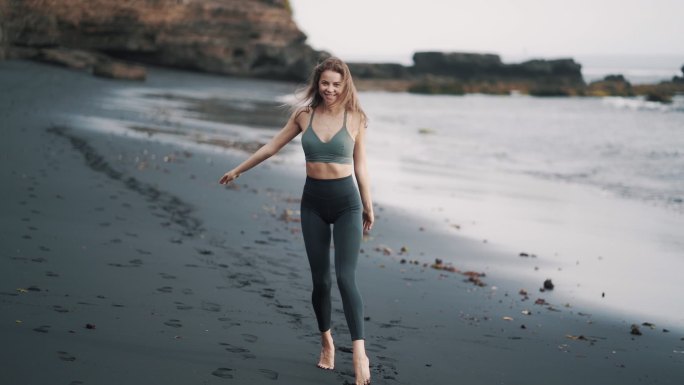穿着运动服的年轻女子沿着黑沙滩散步