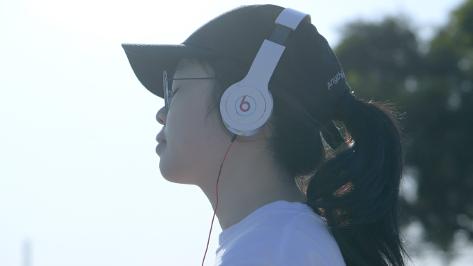 戴着鸭舌帽的女孩在海边用有线耳机听歌