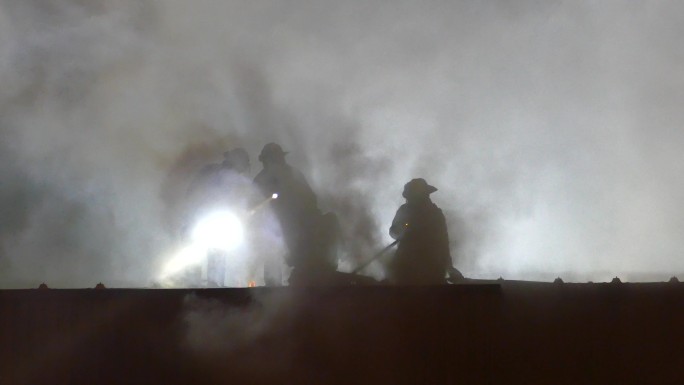 忙碌的消防队员在烟雾缭绕的楼顶上救援