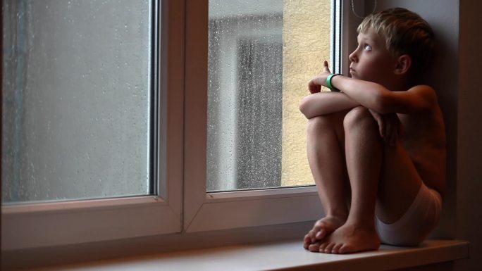 坐在窗边的小男孩安全感蜷缩家庭暴力