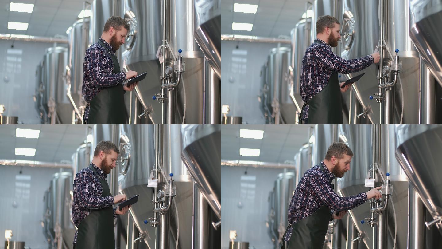一位男性酿酒师站在啤酒罐附近使用平板电脑